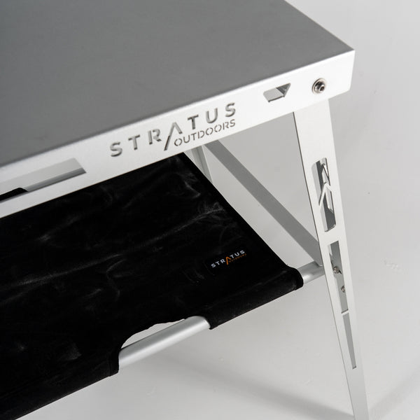 Studio shot of Stratus Outdoors Under Table Hammock highlighting black canvas shelf and white alloy pole supports.